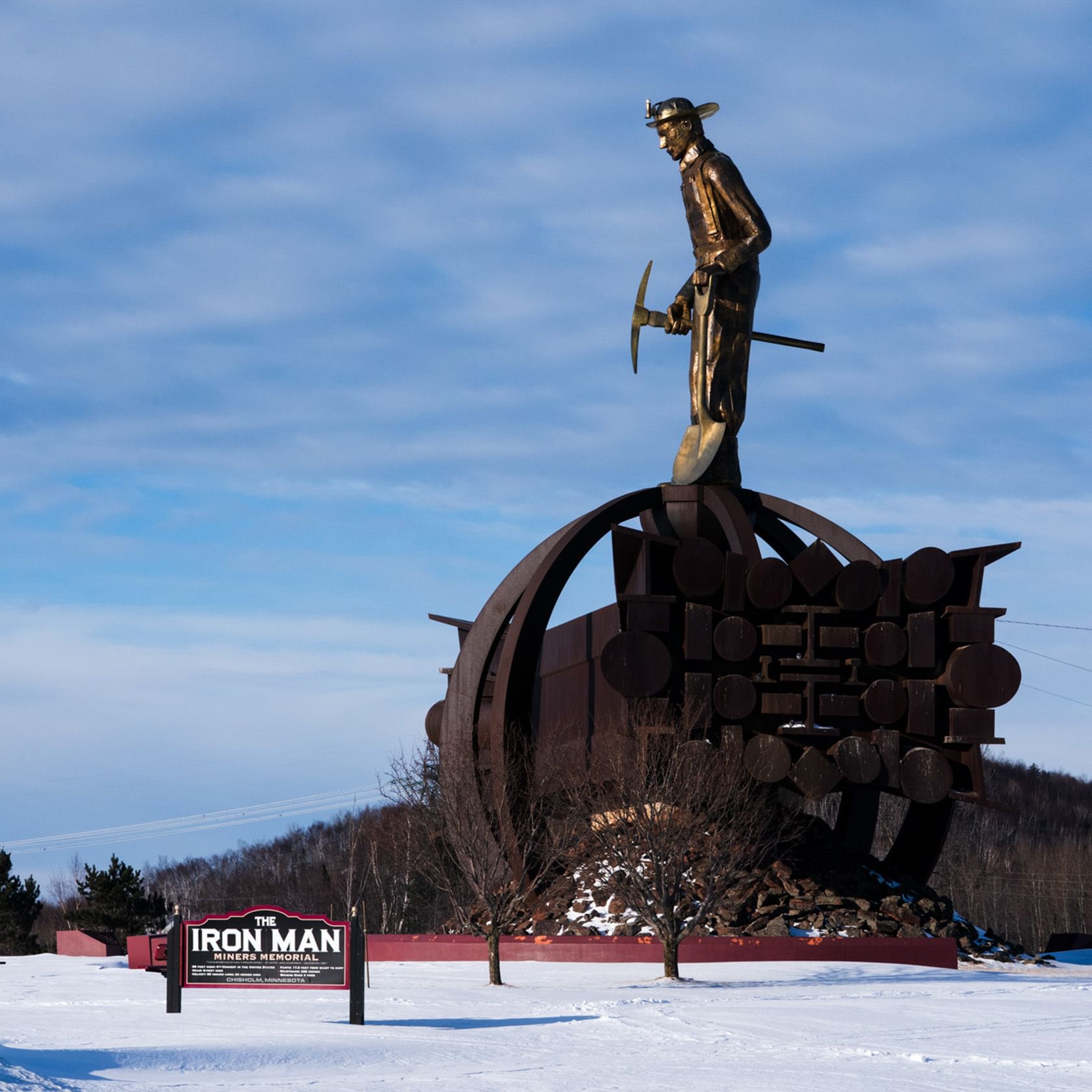 Giant statue of minor in the snow. ﻿Sign says, "The Iron Man Miners Memorial"