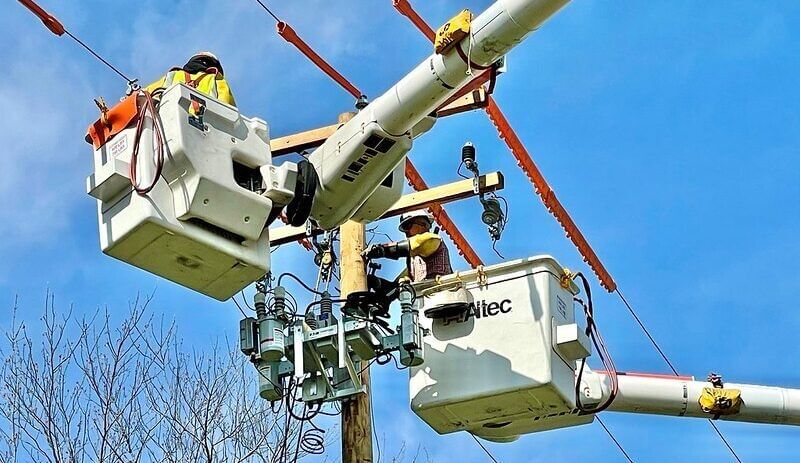 two workers in cherry-pickers working on electric lines