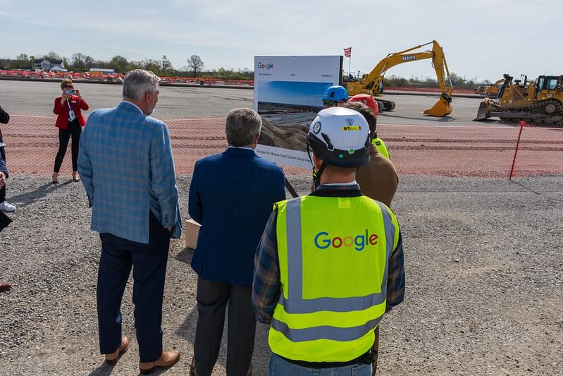 backs of three officials standing outside on asphalt observing forklift and other construction of data center