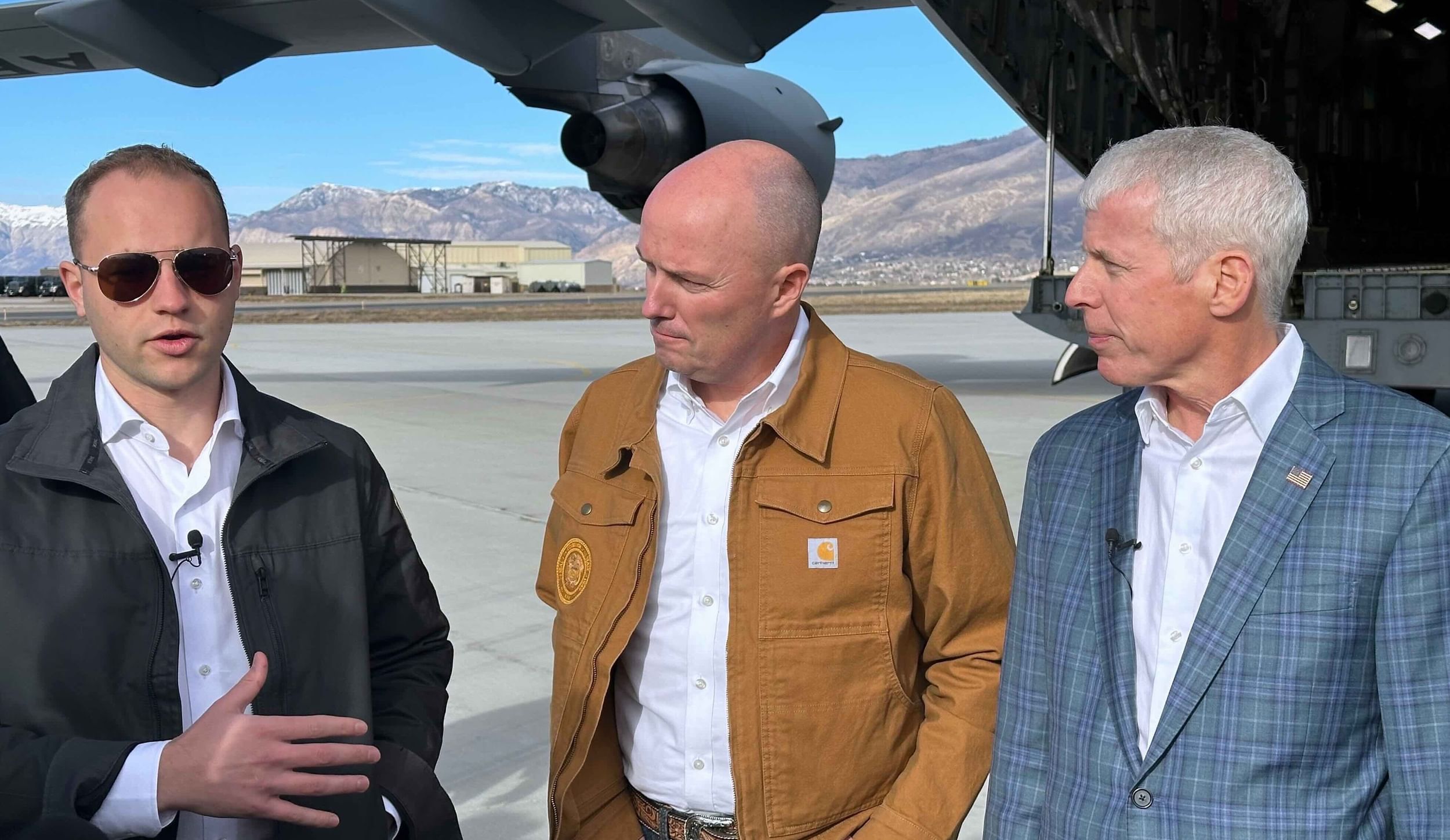 three white guys talking under an airplane wing