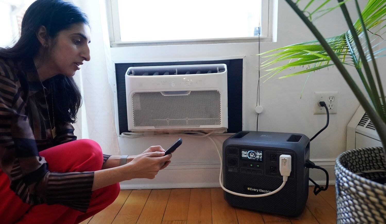 Woman next to air conditioner and battery on light hardwood floor
