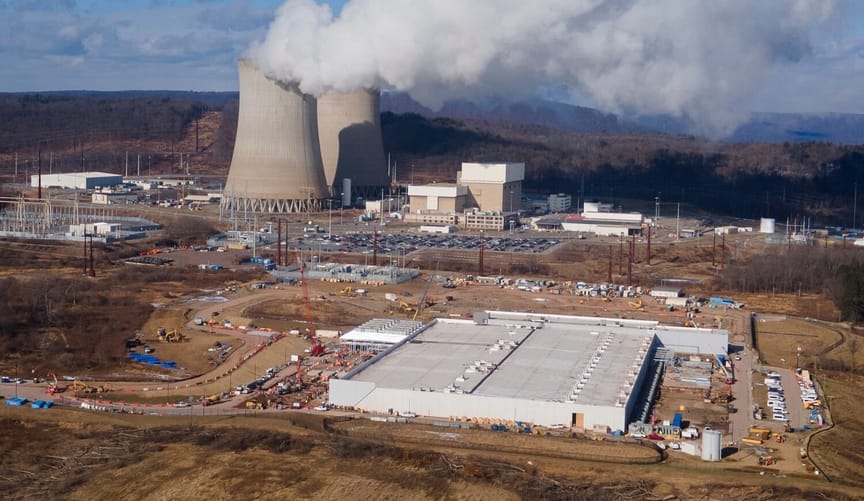 Data center building with construction equipment on a dirt lot, with a nuclear power reactor behind it