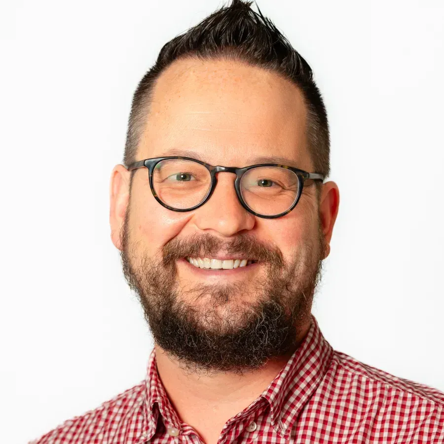 Person in a red-and-white-checked shirt with glasses and a brown beard and mustache