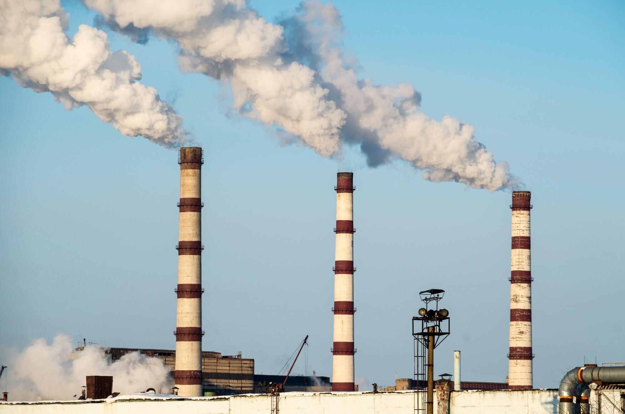 Smoke plumes arise from three tall striped coal stacks at a power plant