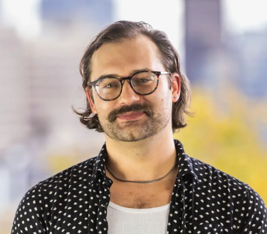Man with chin-length hair and a mustache, wearing glasses wearing polka-dot shirt