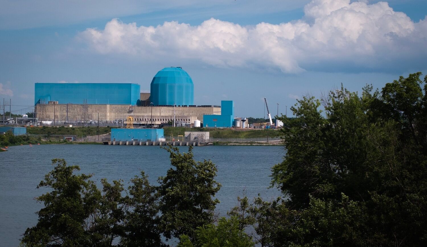 Striking nucleart power plant with light blue dome by a lake, with trees in foreground