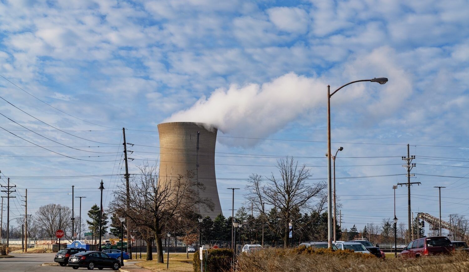 Tower of power plant with cars in front and a cloudy blue sky