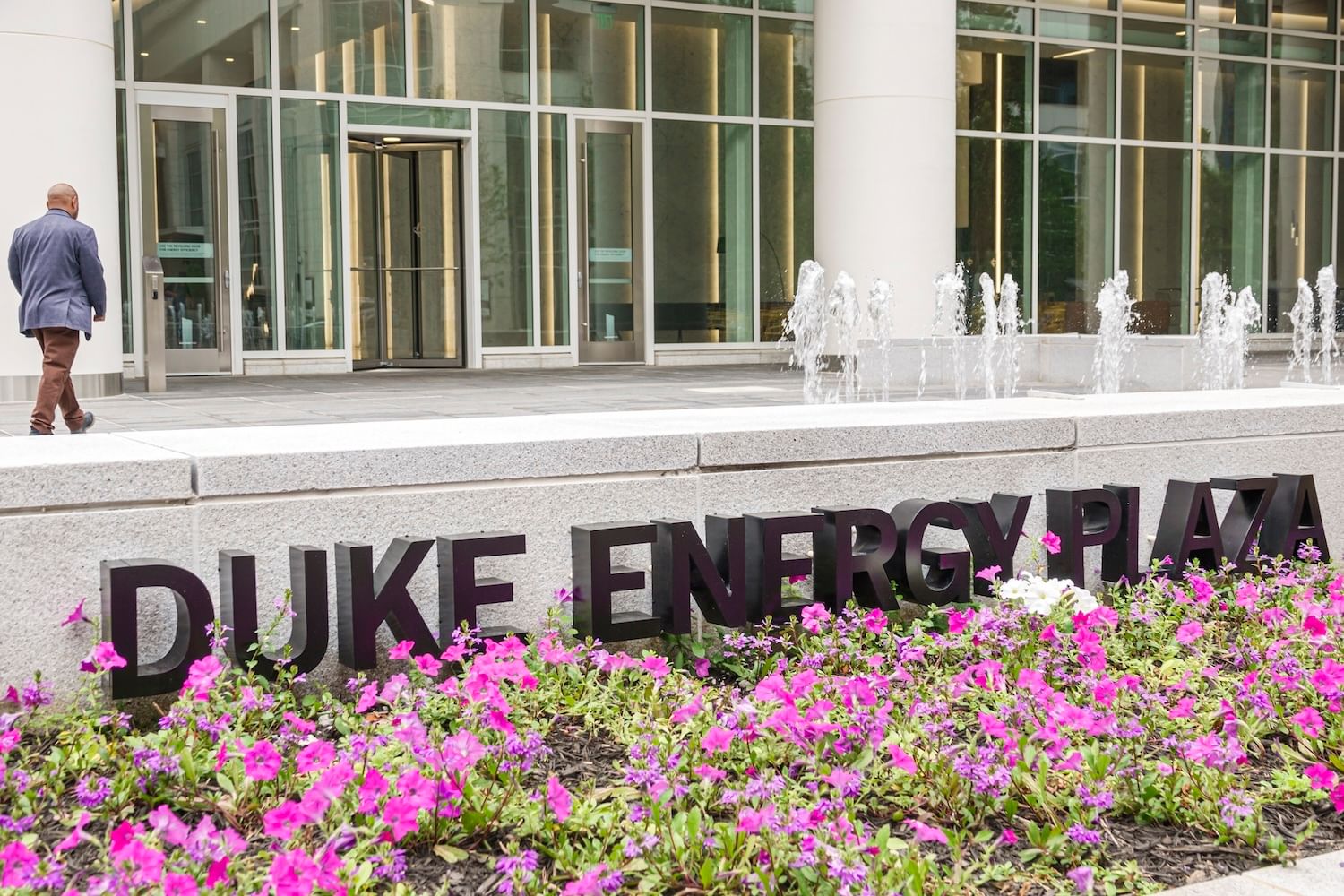 Entryway of building with "Duke Energy Plaza" sign surrounded by purple flowers