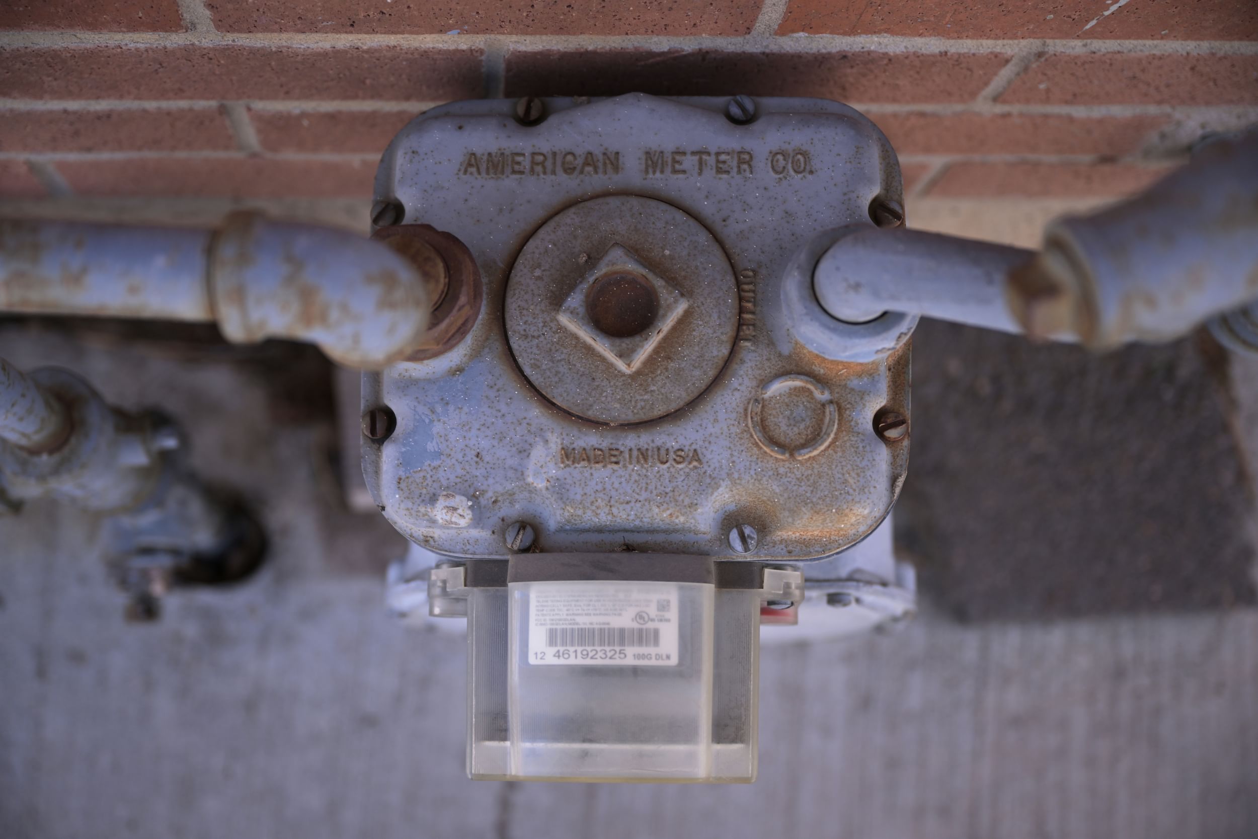 Close-up shot from above of a rusting gas meter from American Meter Co. next to a red brick wall