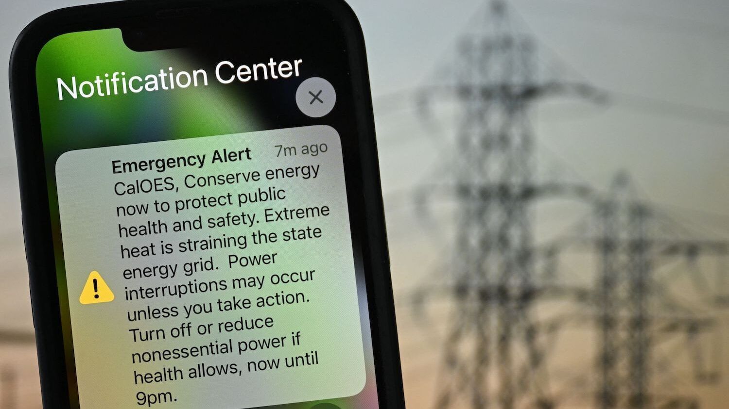 A picture of a smartphone with an emergency alert from the state of California asking residents to curtail power use