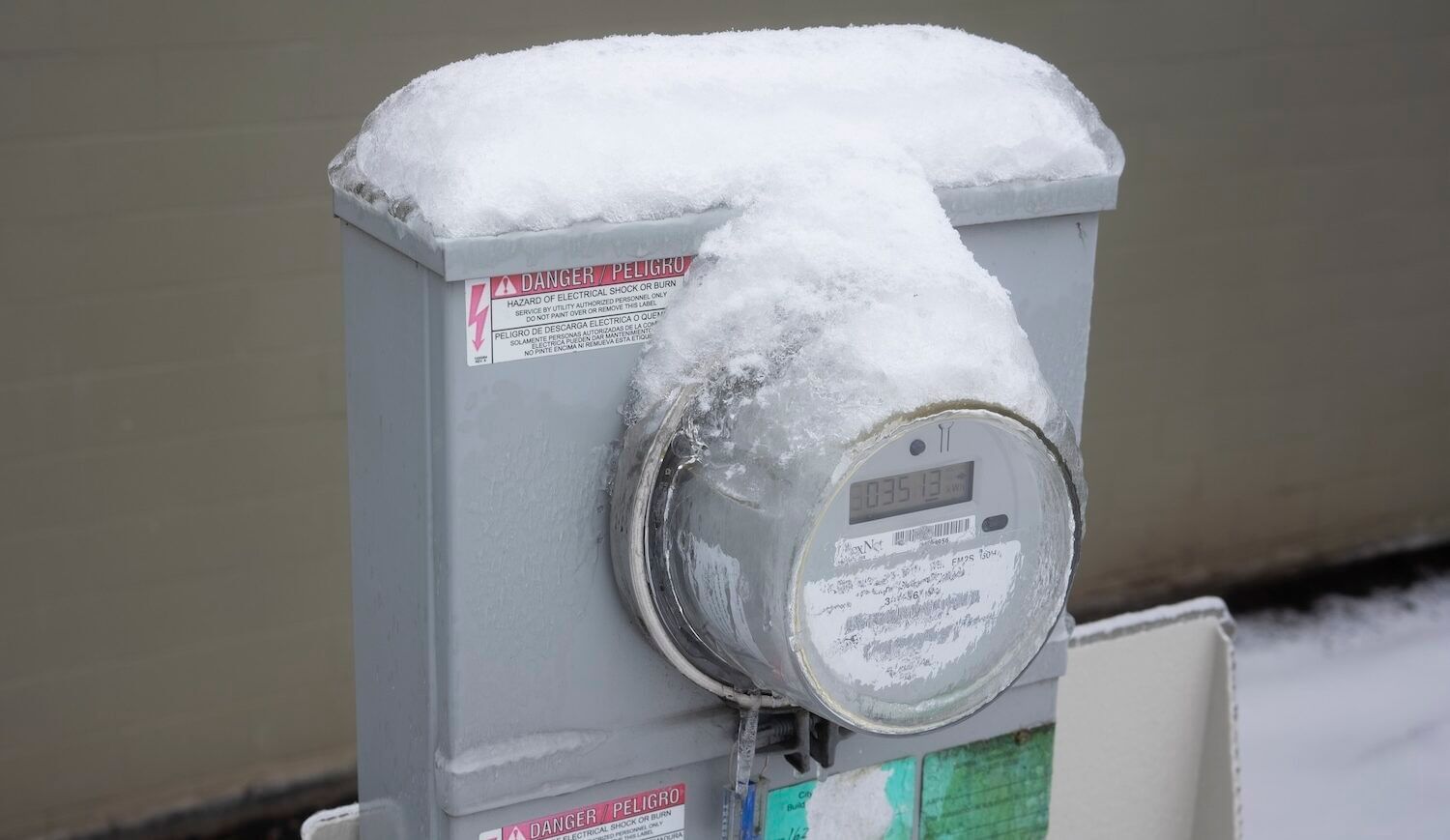 A frozen and snow-covered electricity meter outside a home