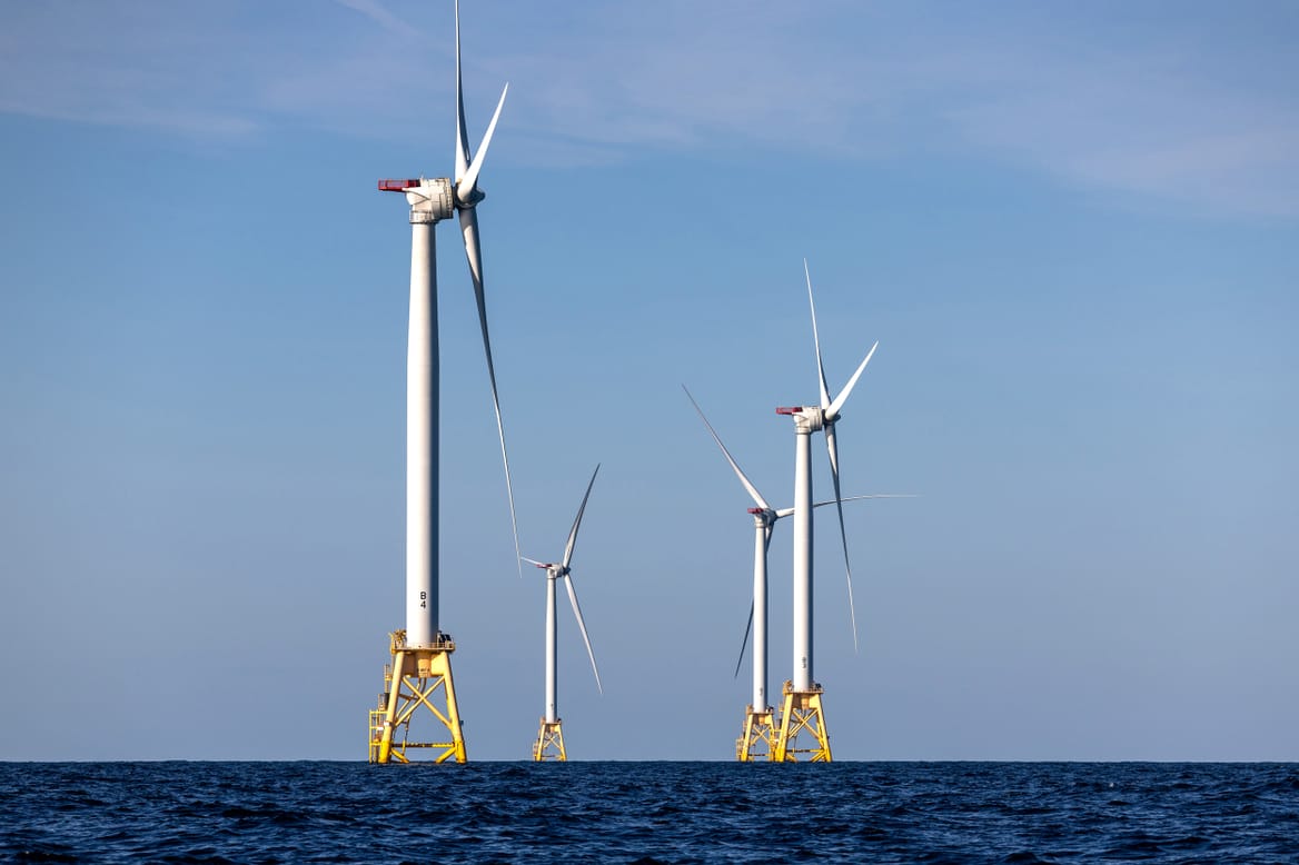 Two wind turbines rise above the ocean.