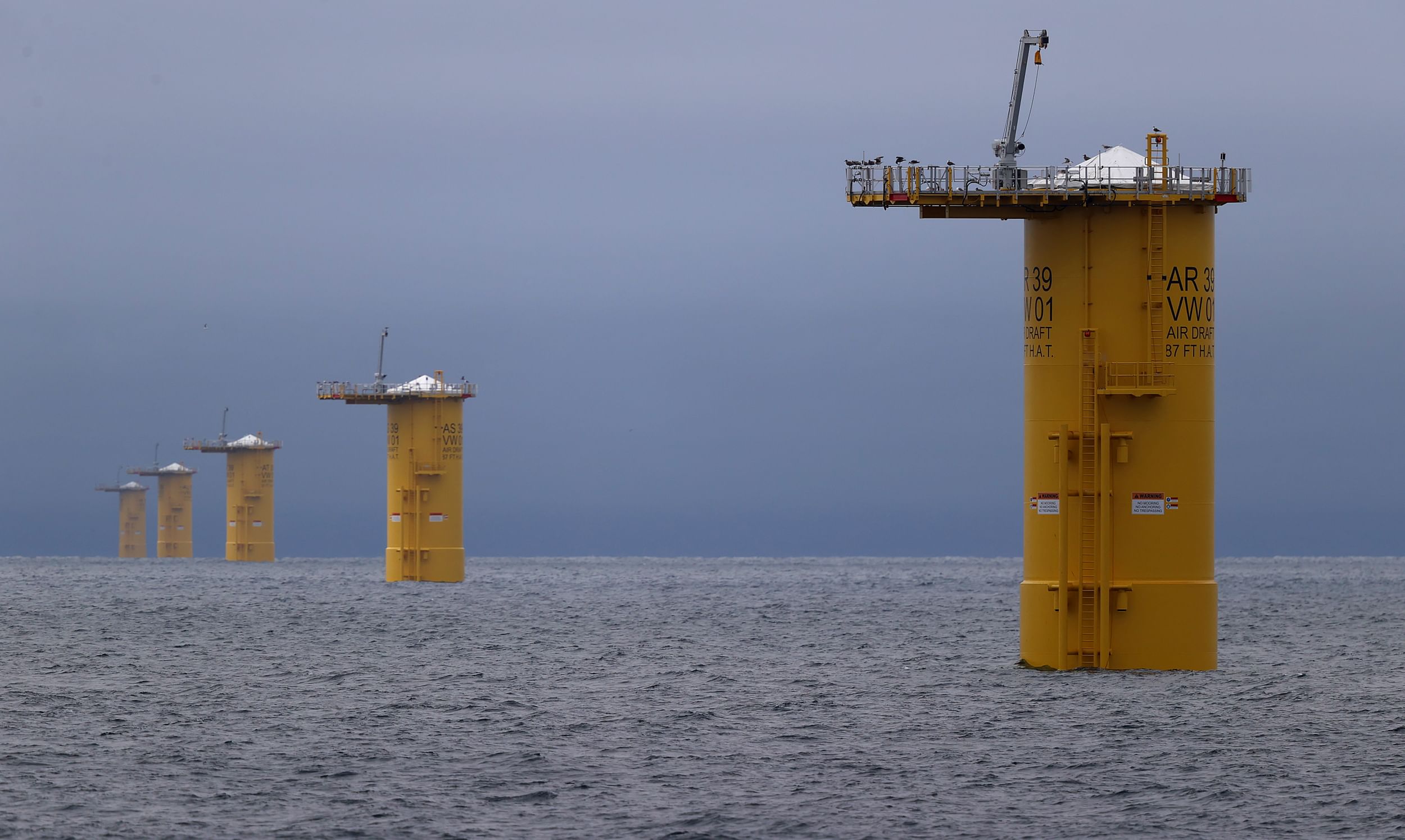 Five yellow bases of wind turbines spread out from near to far in open ocean