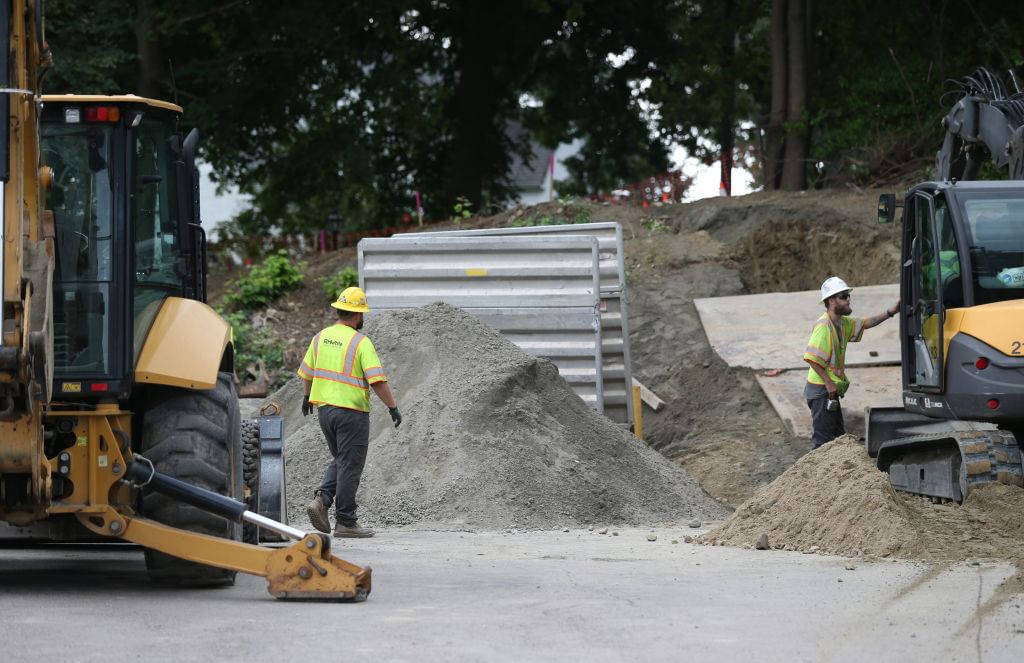 Excavators and two men in construction vests and hard hats at a road being dug up