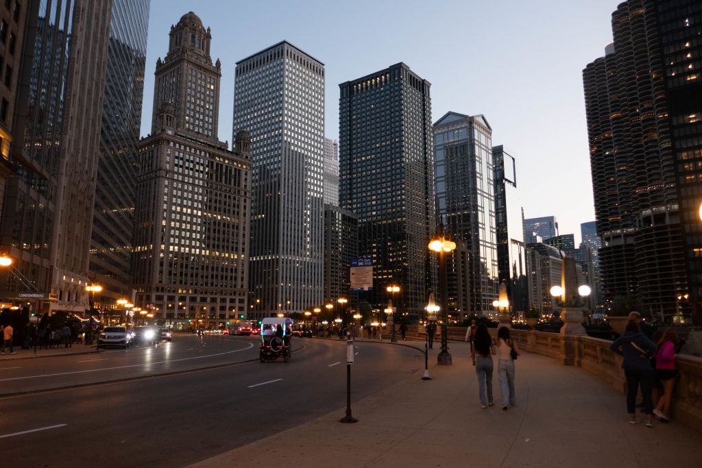 road, sidewalk, some pedestrians and big buildings at dusk