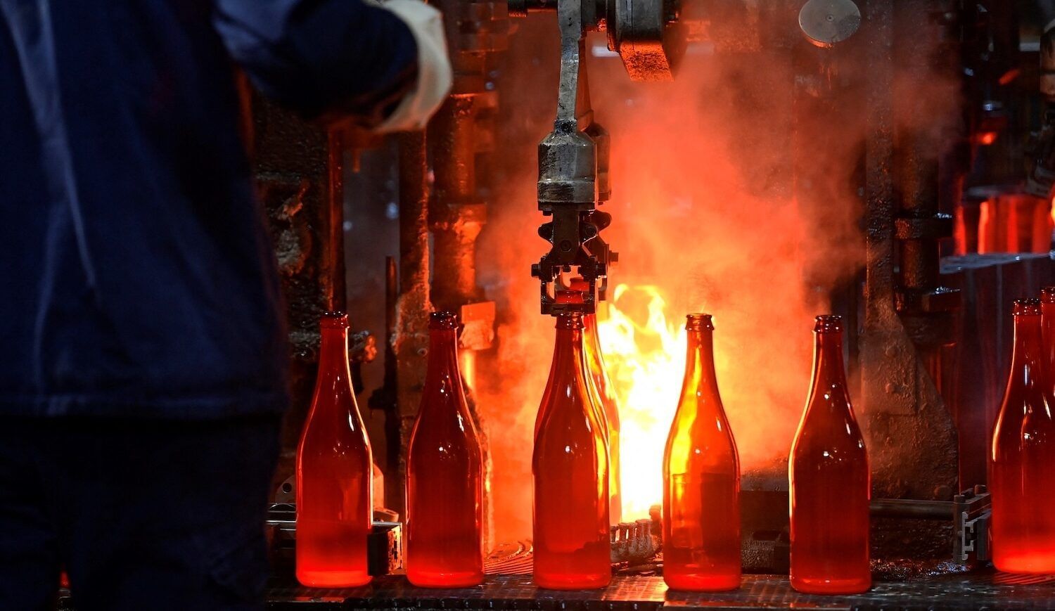 Glass bottles lined up along industrial equipment, with hot flames in background