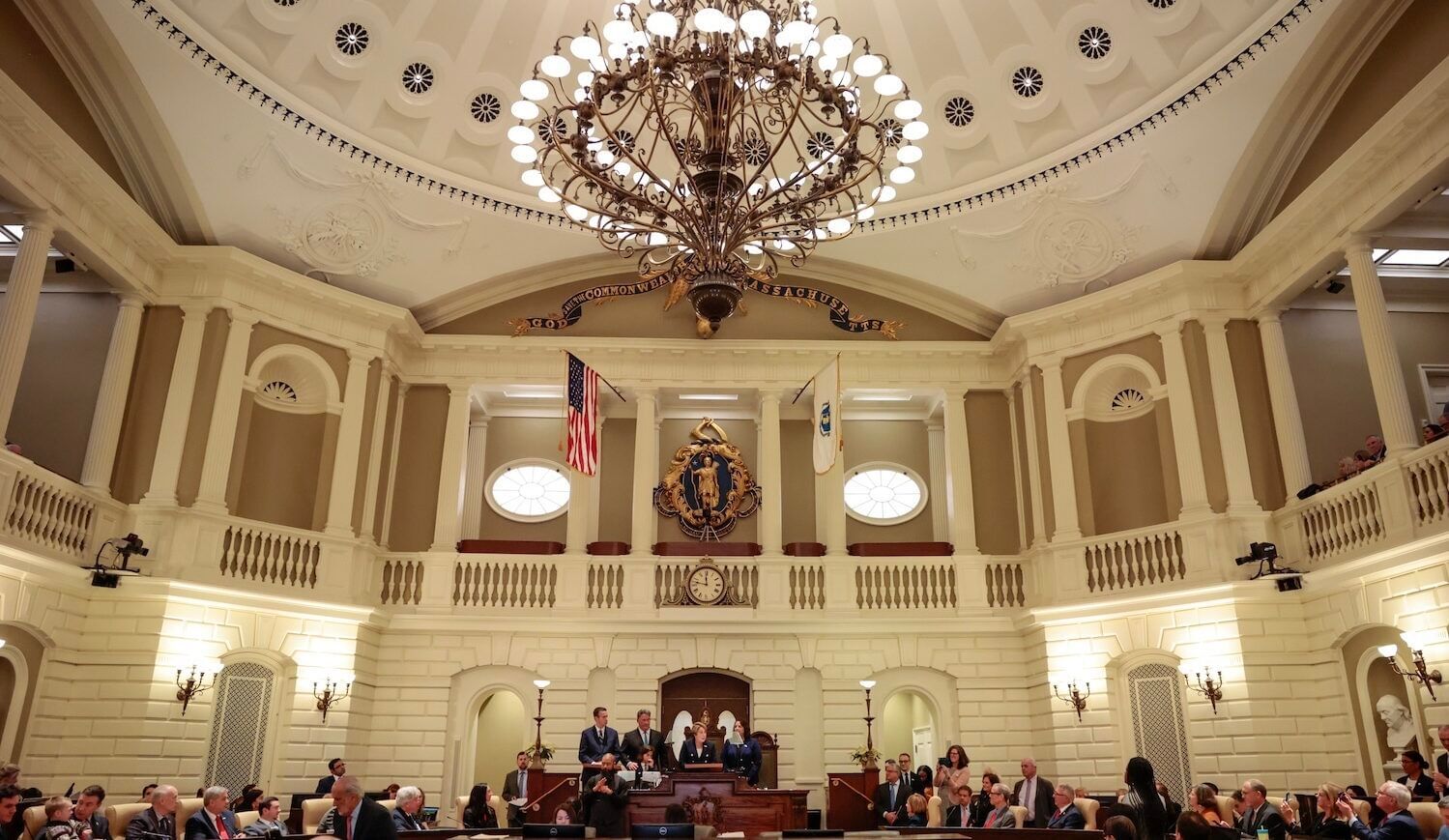 People in business attire gather in a large room with a large chandelier