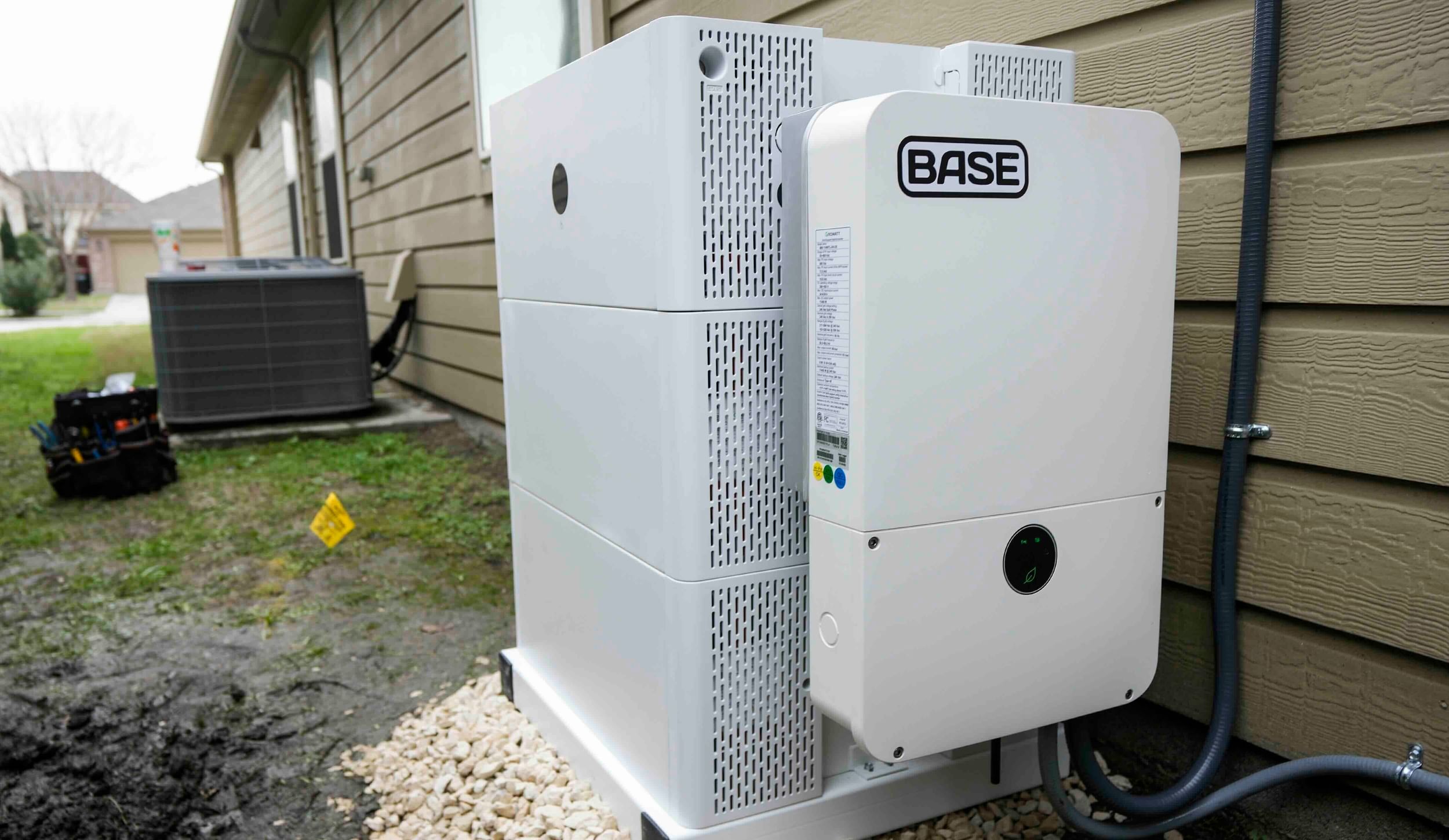 A white battery box with "Base" on it, adjacent to a house