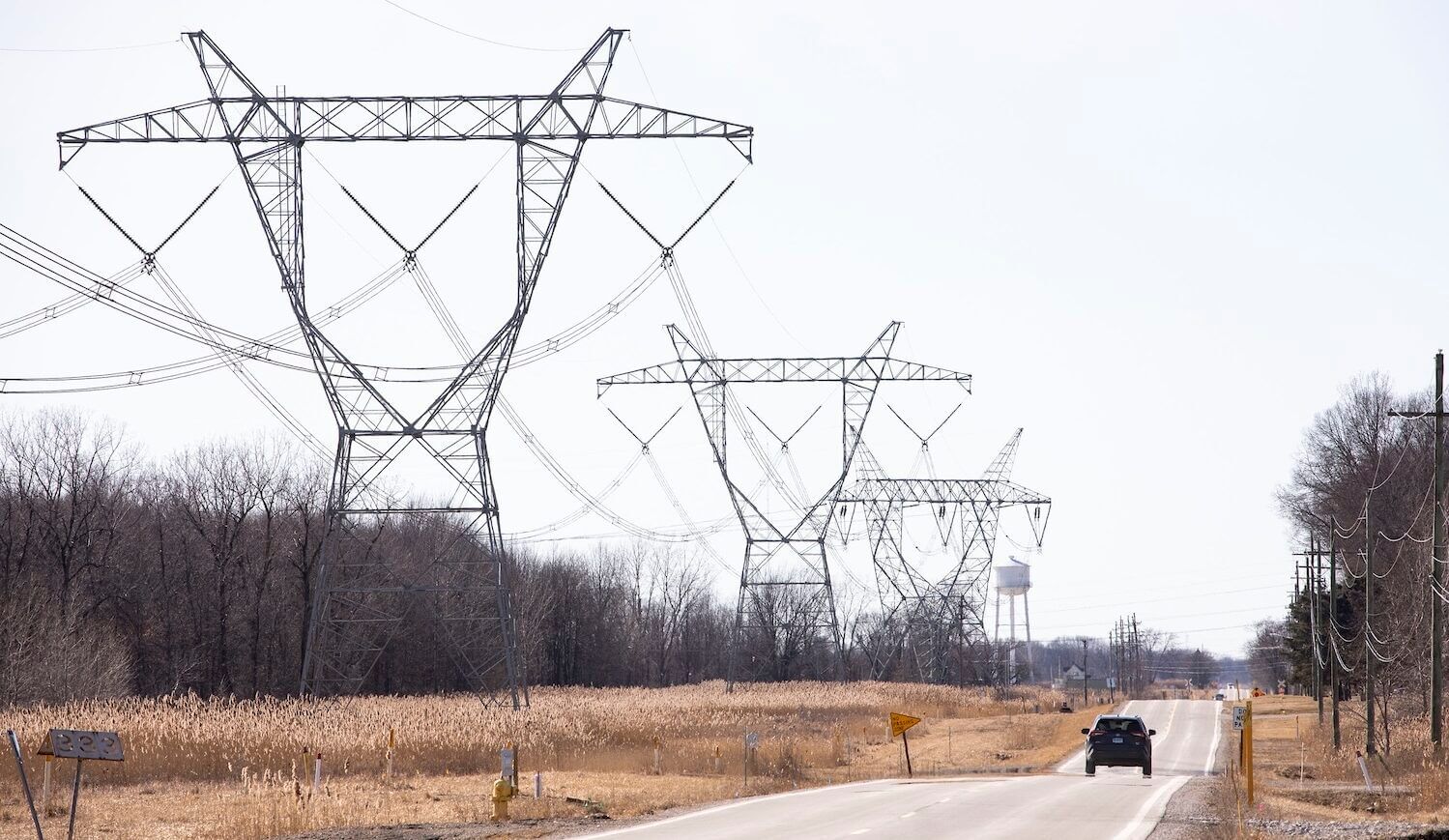 A car drives down a road alongside transmission towers and wires