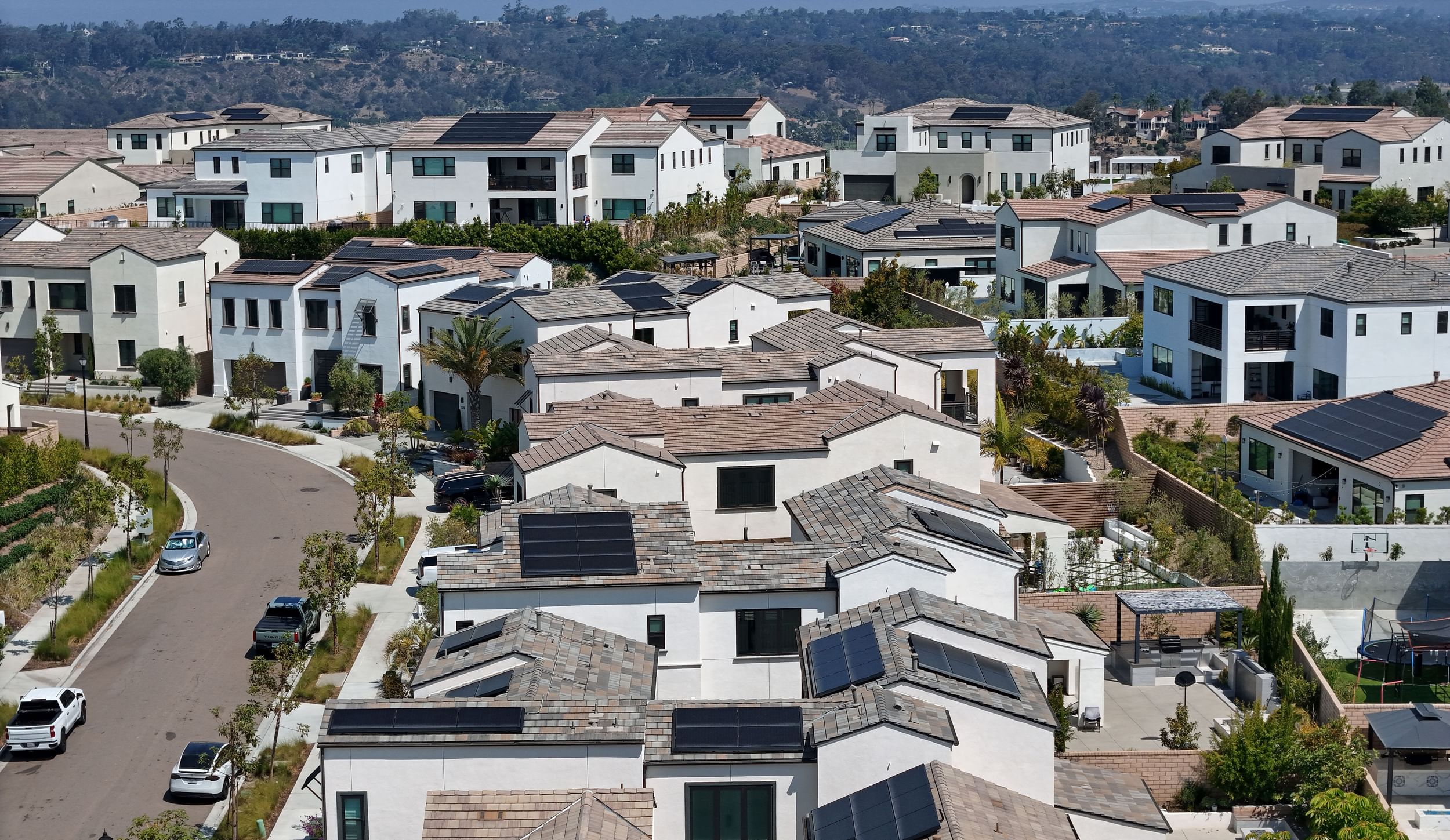 Curved residential street in a neighborhood of two-story homes showing many roofs with solar panels