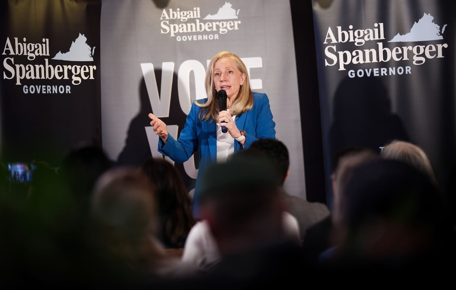 A woman speaks into a microphone in front of signs that say "Abigail Spanberger governor"
