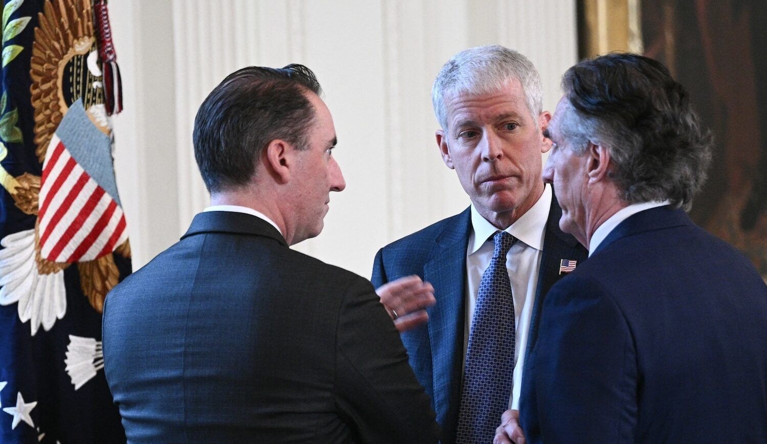 Three men in suits speak