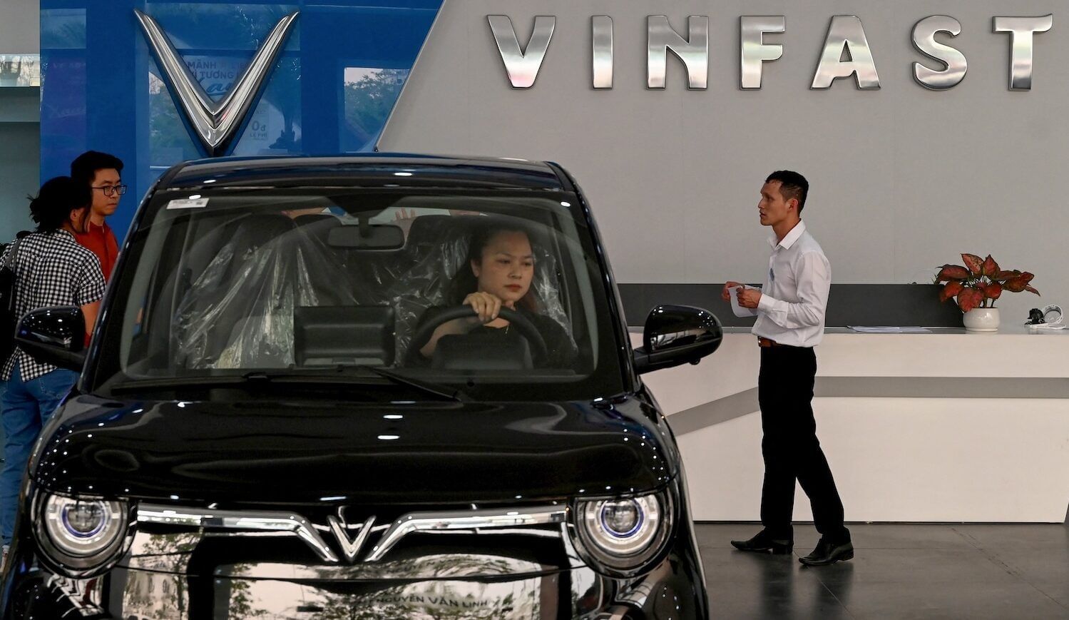 Woman sitting in a new EV in a car dealership in Hanoi with "Vinfast" sign behind her