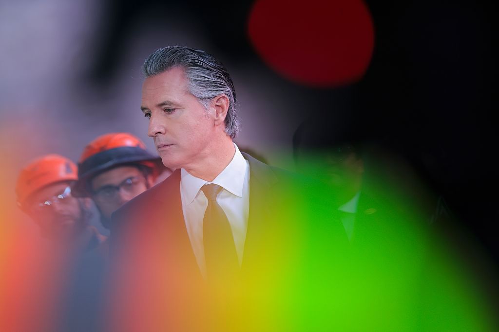 California Governor Gavin Newsom wearing suit and tie, looking to left, with blurry green and red dots in foreground