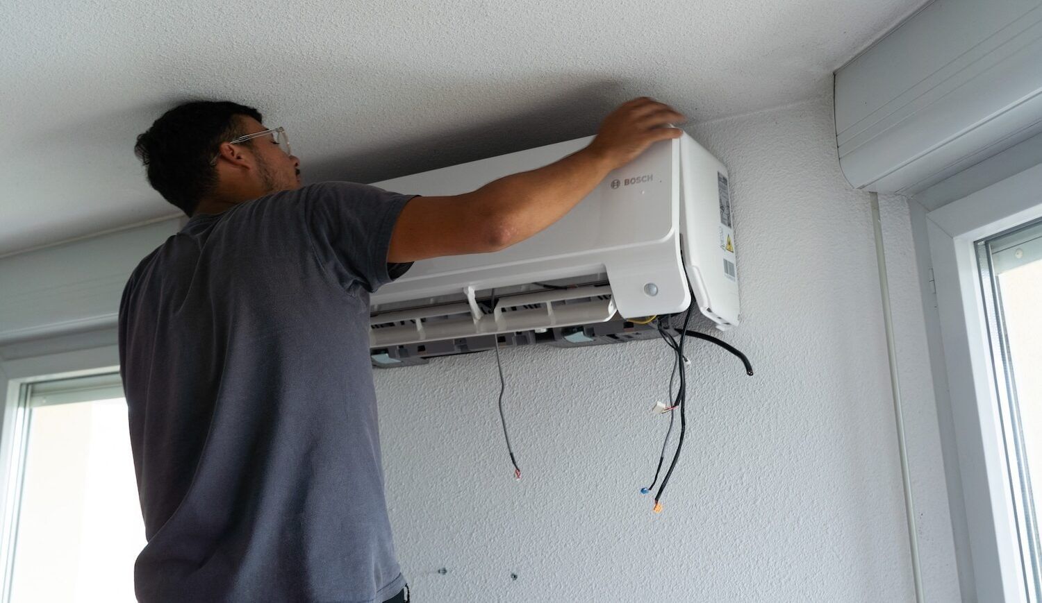 A person holds HVAC equipment on an empty wall