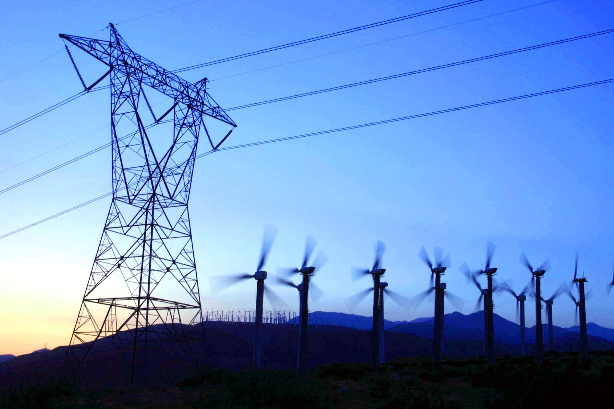 Wind turbines and a transmission pylon against a blue sky