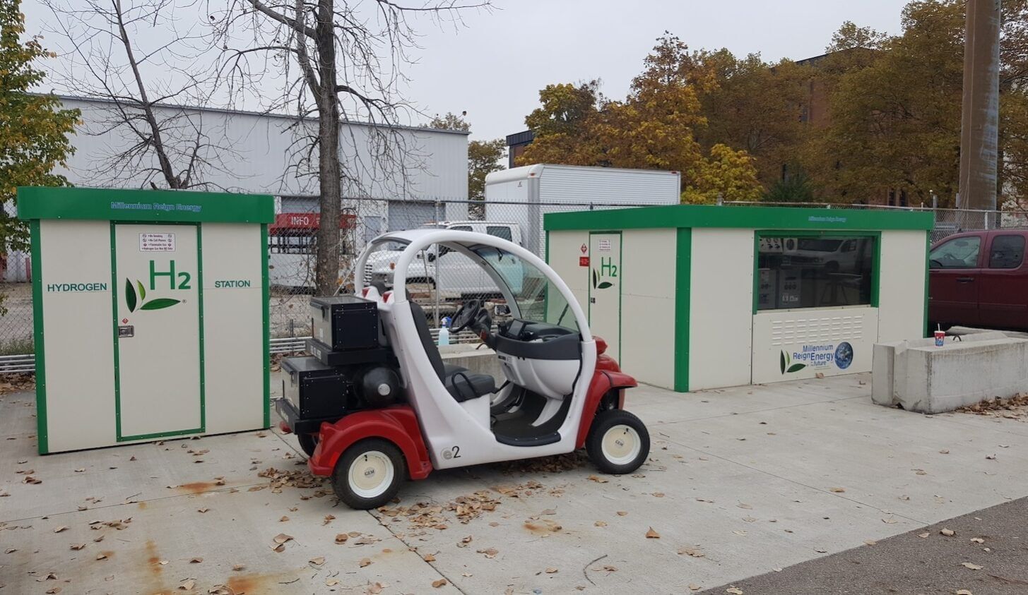 A small vehicle parked in front of a small shed with the word "H2" printed on it.