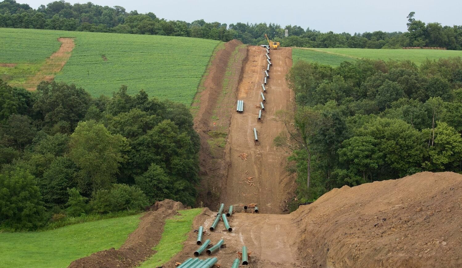 Pipes laid out along a line of dirt surrounded by grass and trees