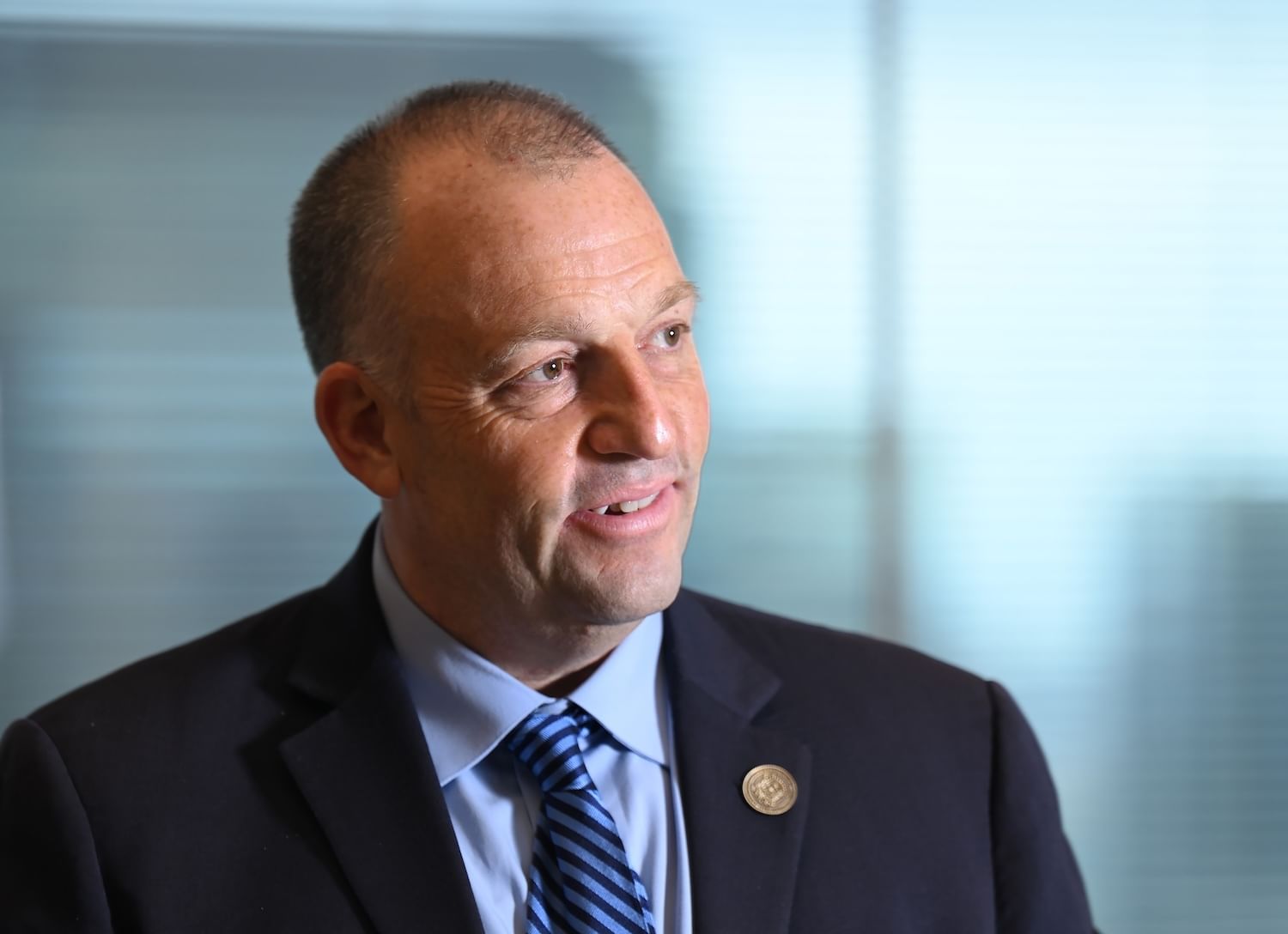 Man in a dark suit, light-blue shirt, blue striped tie