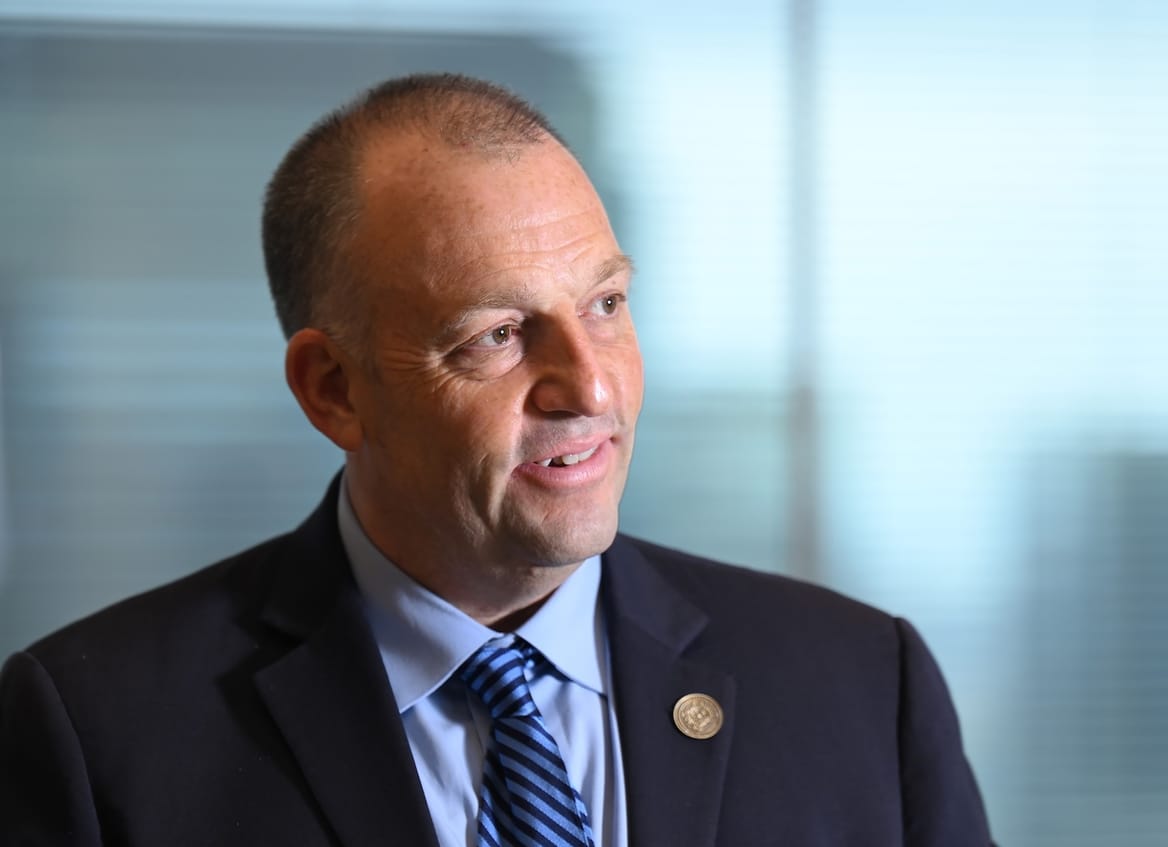 Man in a dark suit, light-blue shirt, blue striped tie