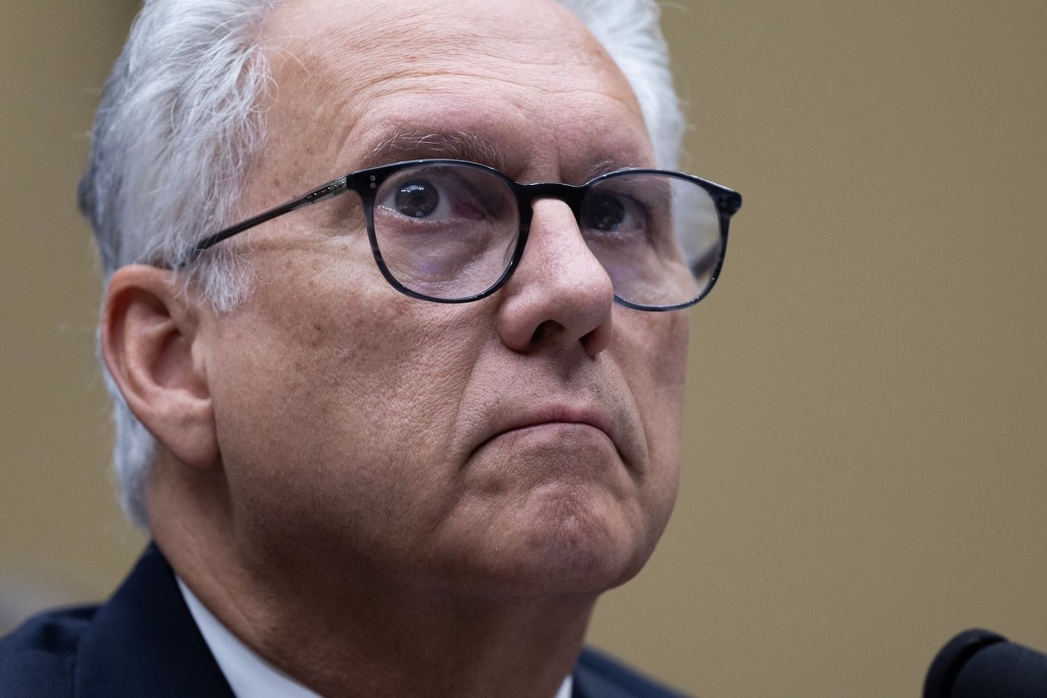 Head of man with white-gray hair and dark-rimmed glasses