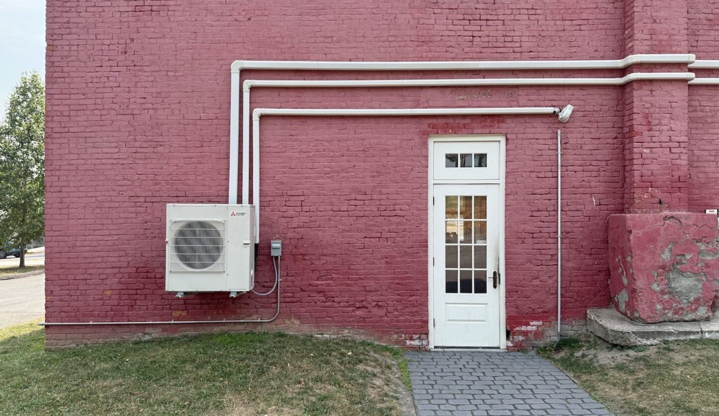 HVAC equipment on the side of a red brick building with a white door