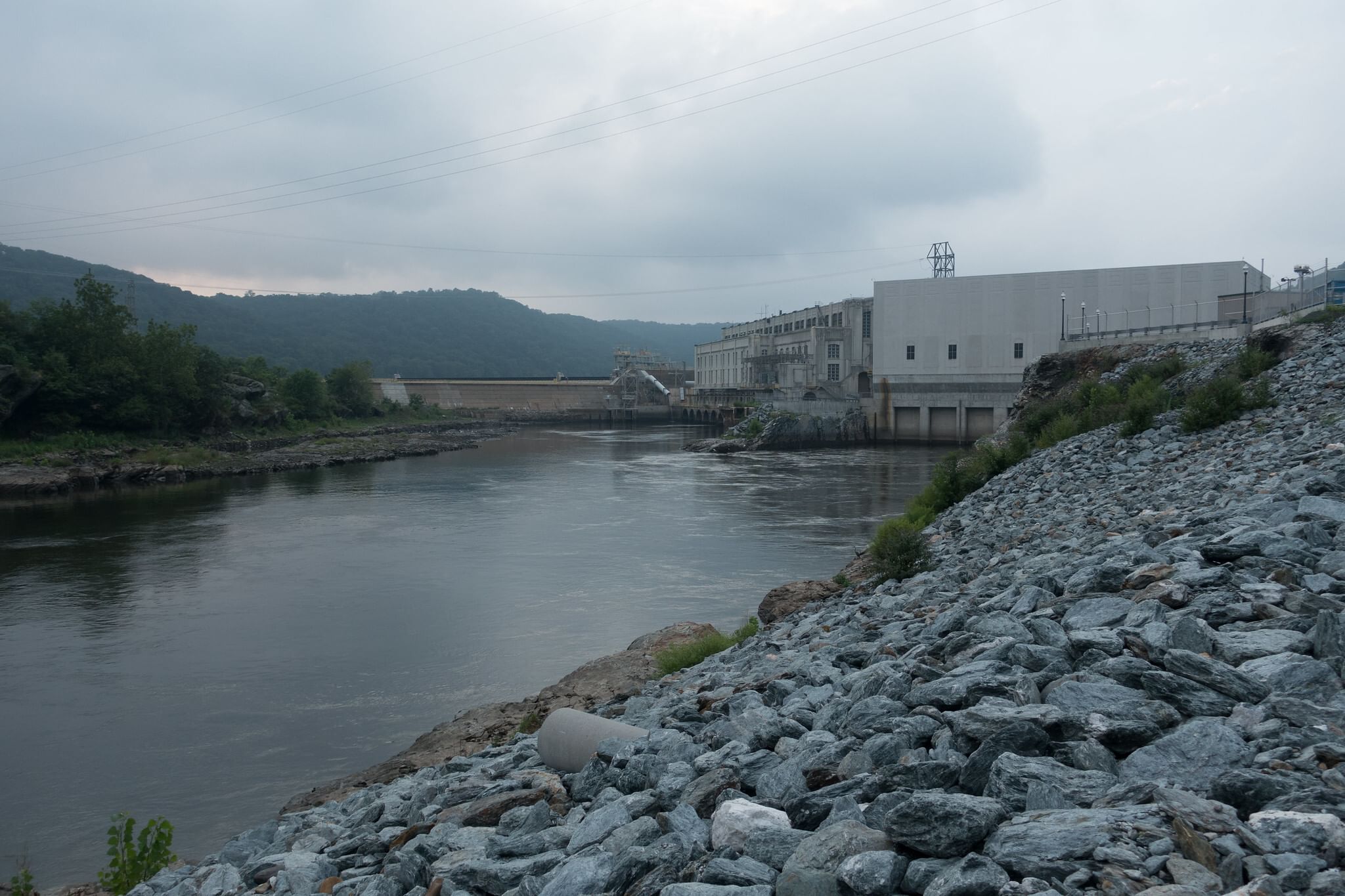 Dam by a river in Pennsylvania on an overcast day, with rolling hills in the background and a rocky shore in the foreground