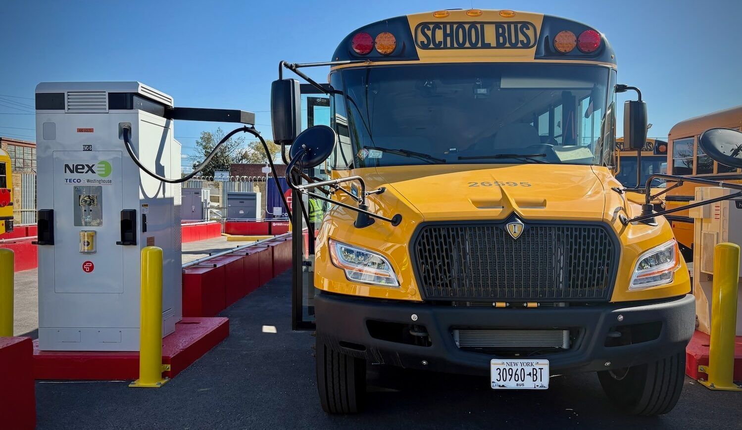 Yellow school bus plugged into a white battery with a red base seen from the front