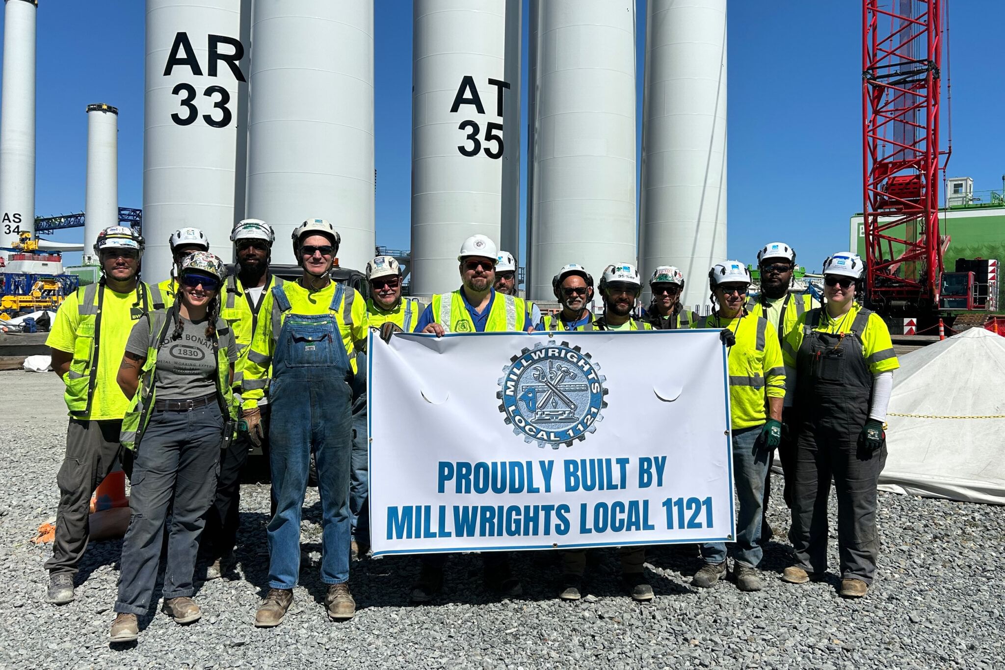 A group of Millwrights Local 1121 workers in hard hats stand in front of wine turbine towers.