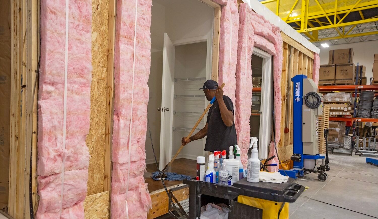 Worker mops a floor in modular unit, with plywood and pink insulation on its outside walls