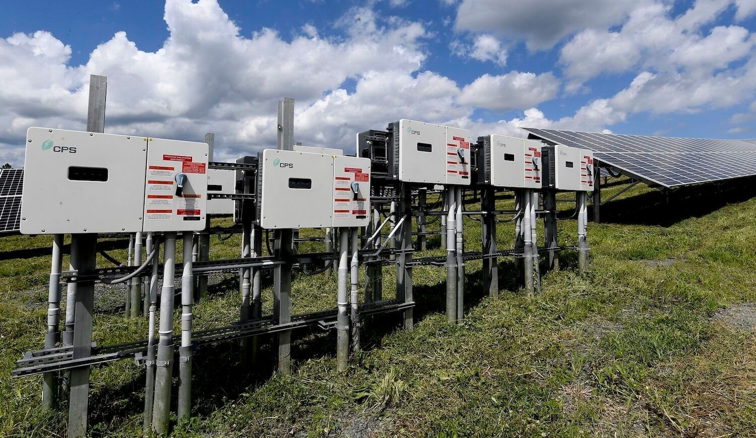 Inverters and solar panels on a grassy plot under a blue sky