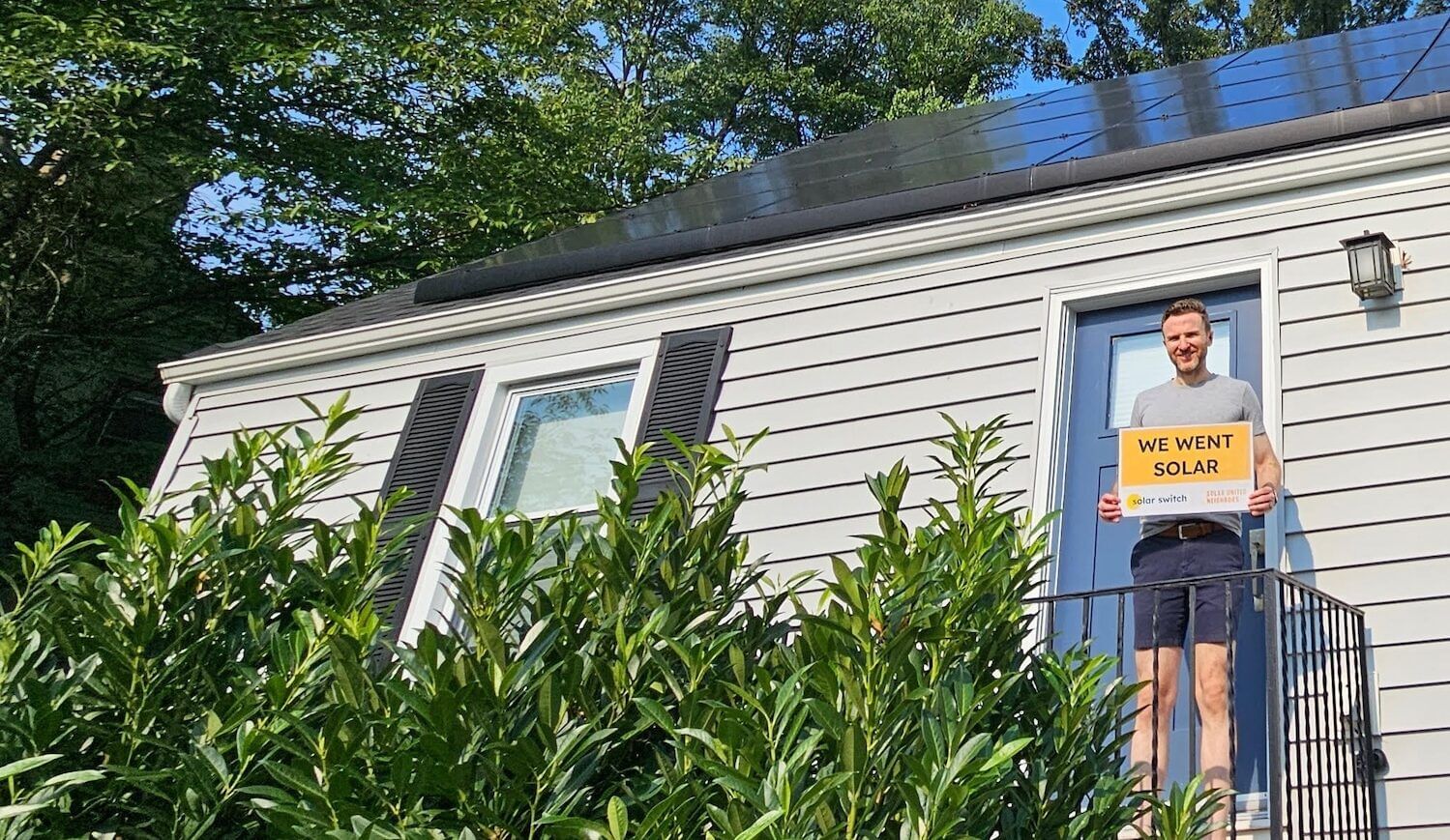 Man stands on porch with "We Went Solar" sign