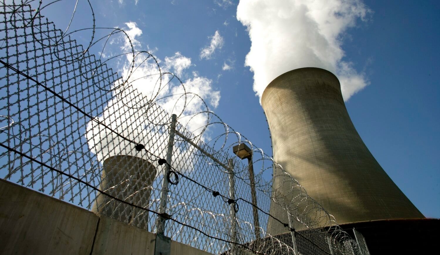Two nuclear cooling towers with steam and a security fence, shot from below