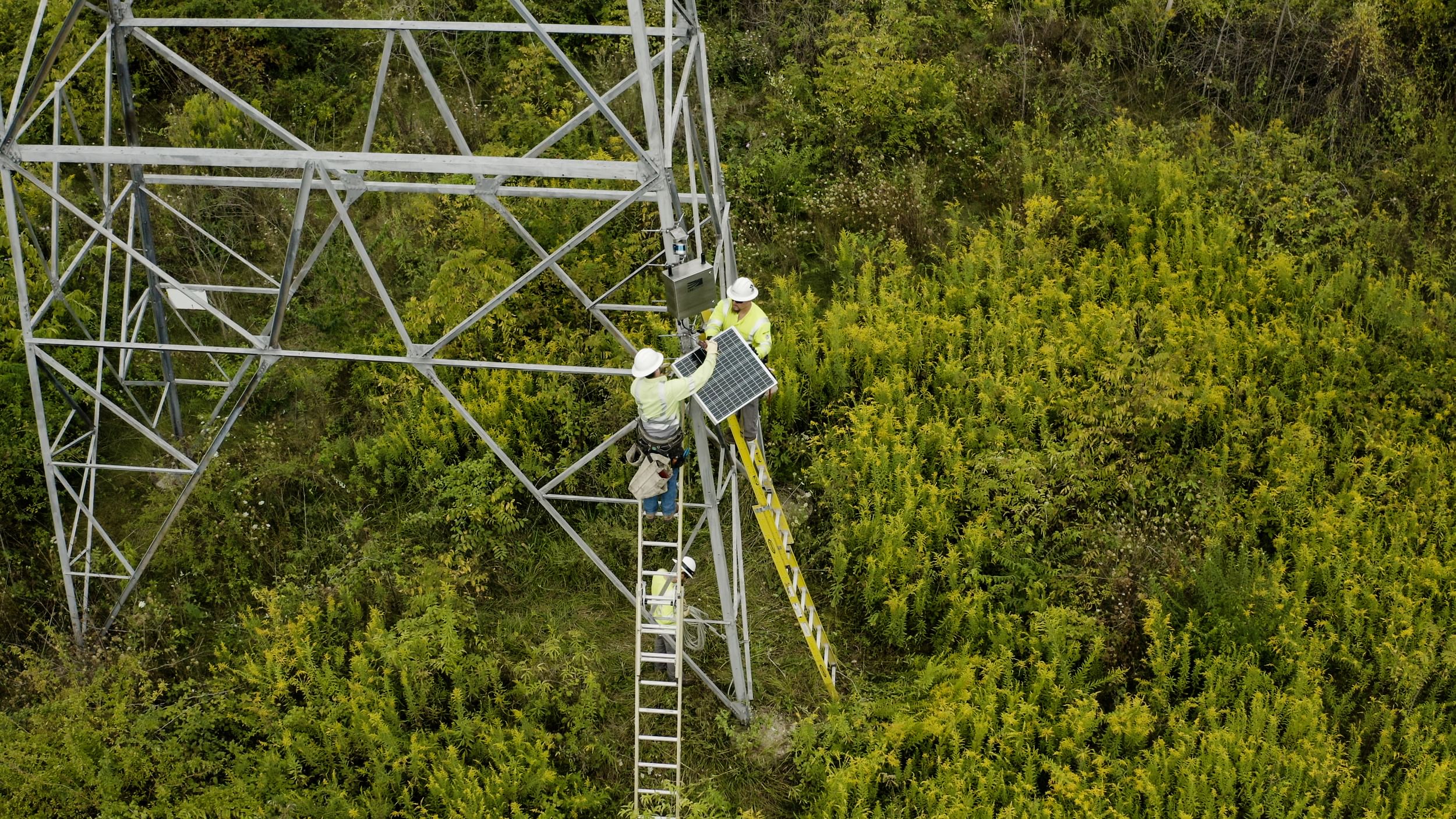 Workers install a LineVision dynamic line rating sensor at the base of a transmission tower.