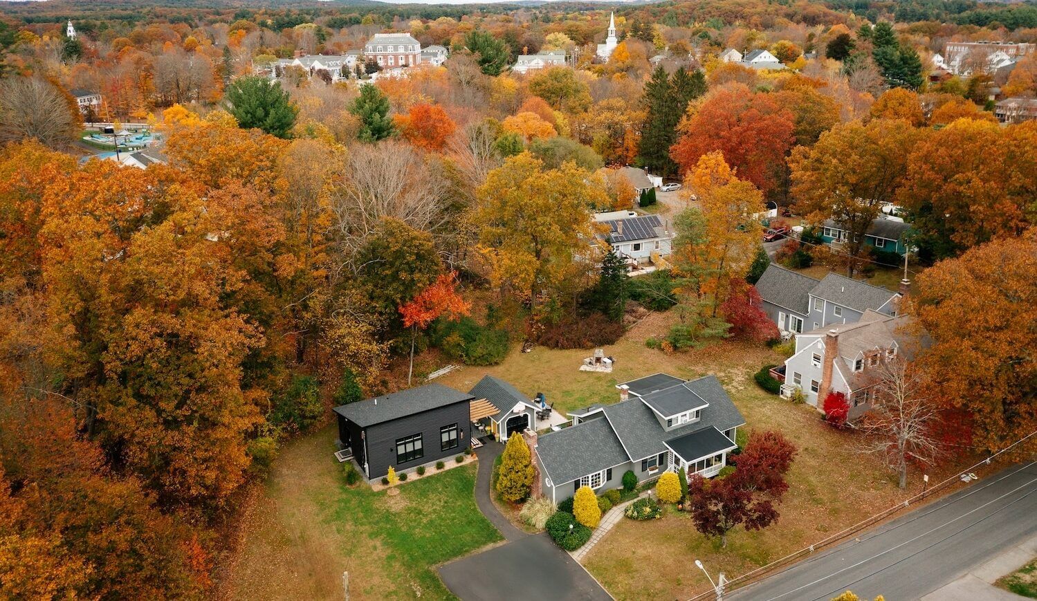 Overhead shot of gray house with dark gray ADU in backyard surrounded by trees in fall color