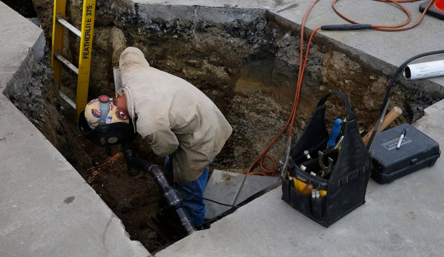 Hard-hatted worker below concrete ground next to yellow ladderw