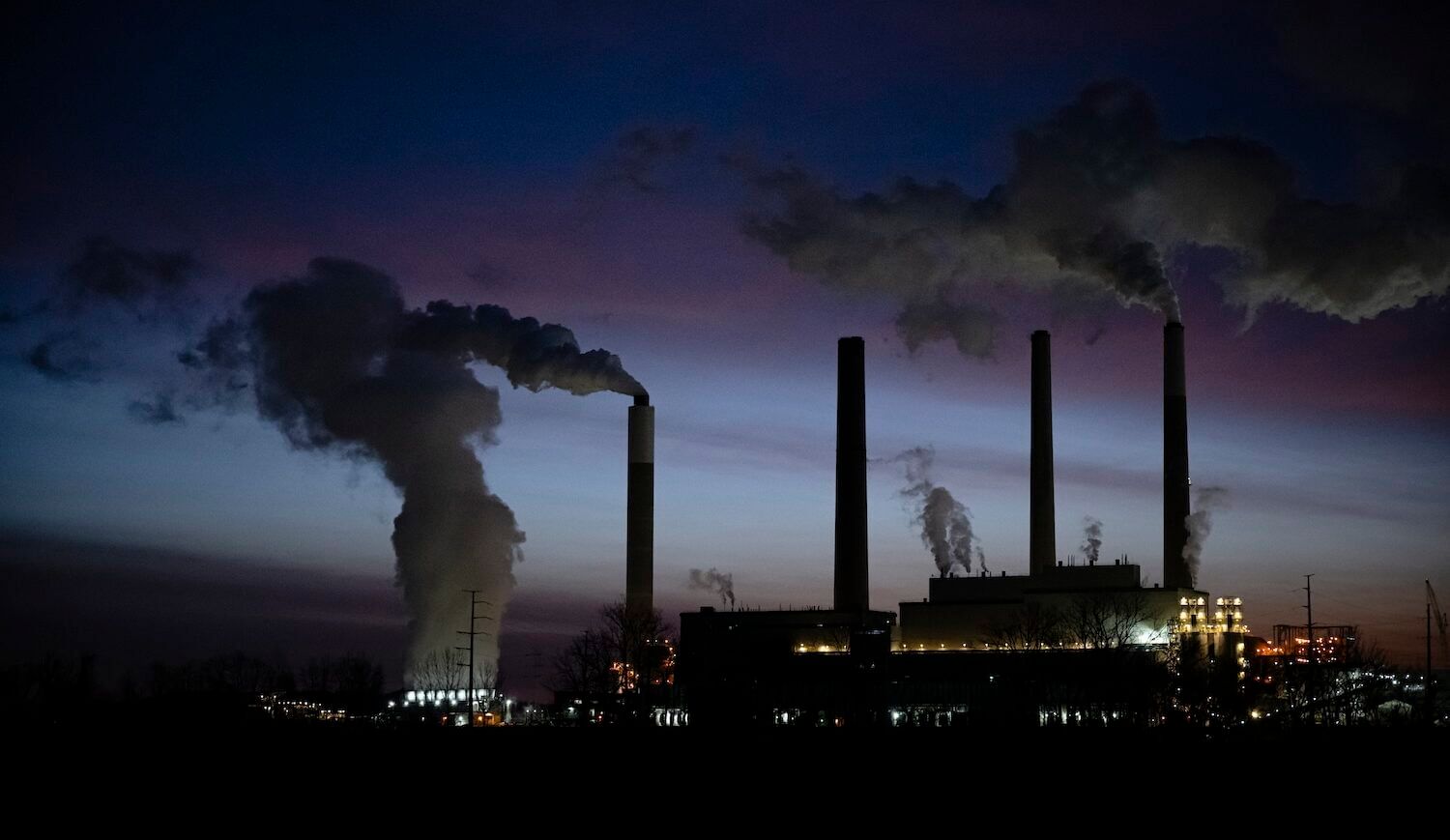 Coal plant lit up at dusk with four stacks, some billowing smoke
