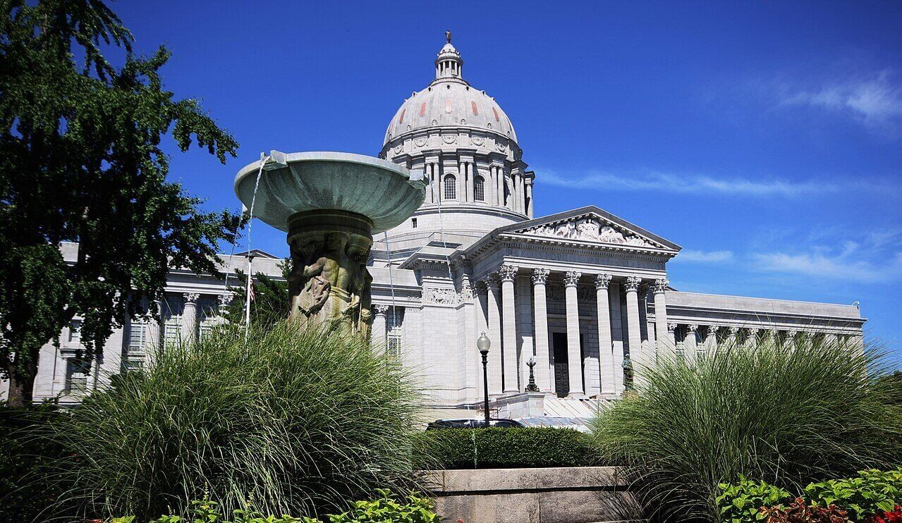 Traditional-style state capitol building with plantings in front and a blue sky behind