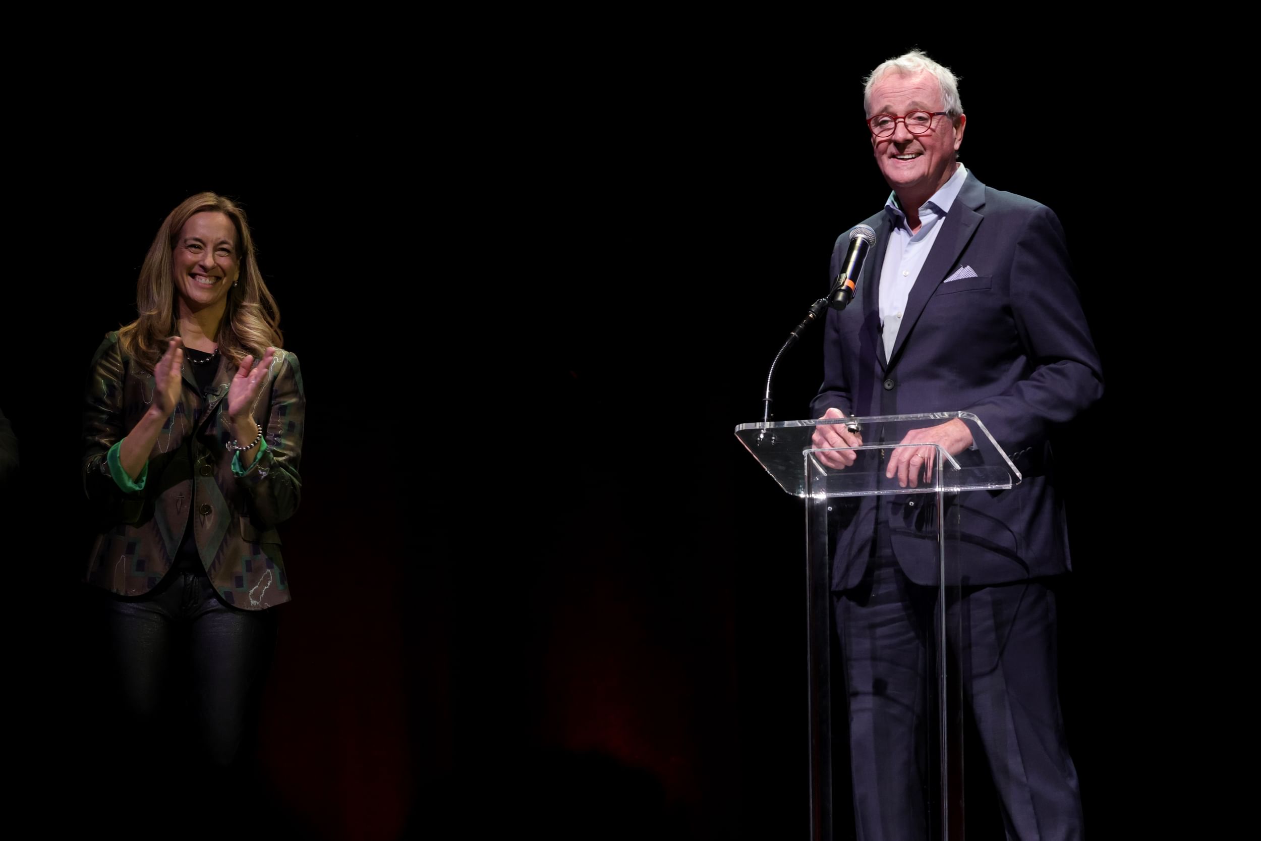 Sherrill, on the left, applauds Murphy, who stands before a clear podium with a microphone.