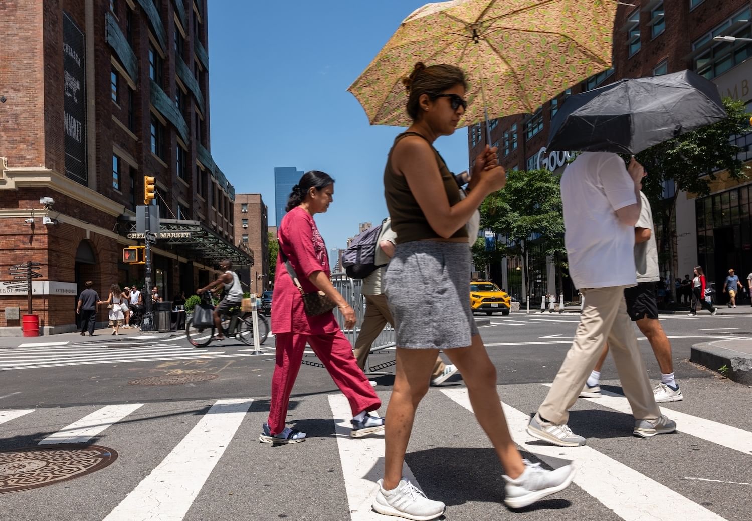 Two people holding umbrellas at a crosswalk by the red-brick Chelsea Market